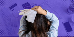 Una persona tomándose la cabeza con angustia mientras sostiene varias facturas sobre un escritorio lleno de tarjetas de crédito y documentos de cobro.